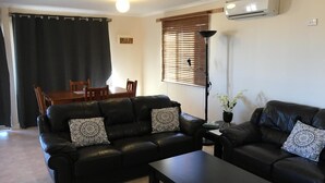 A living room with two black leather sofas, a coffee table, a dining table with chairs, and a window with blinds. - Airport Whyalla Motel (Whyalla Norrie)