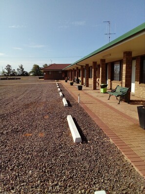 A building with a covered walkway, outdoor seating, and a gravel area. - Airport Whyalla Motel (Whyalla Norrie)