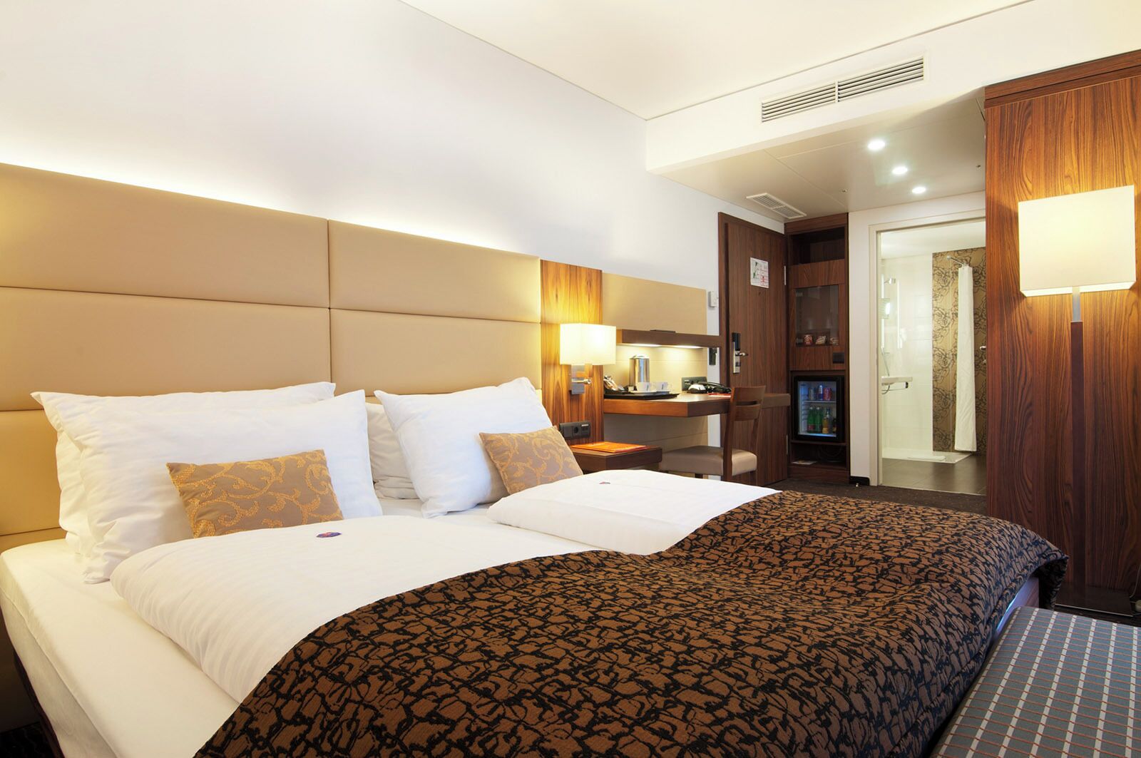 Une chambre d’hôtel avec un grand lit, un bureau avec une chaise, un petit réfrigérateur et un espace douche.