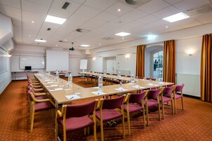 Una sala conferenze con lunghe tavolate, sedie e una lavagna.