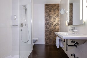 Uma casa de banho moderna com cabine de duche em vidro, sanita e lavatório com espelho.