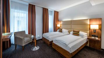 A hotel room with two beds, a desk, a chair, and a small table.