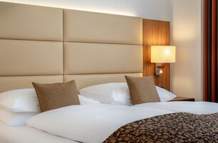 A hotel room with a large bed, a headboard with a light fixture, and a wooden panel on the wall.