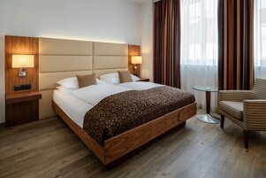 Ein Hotelzimmer mit einem großen Bett, zwei Nachttischen mit Lampen, einem kleinen runden Tisch und einem Stuhl.
