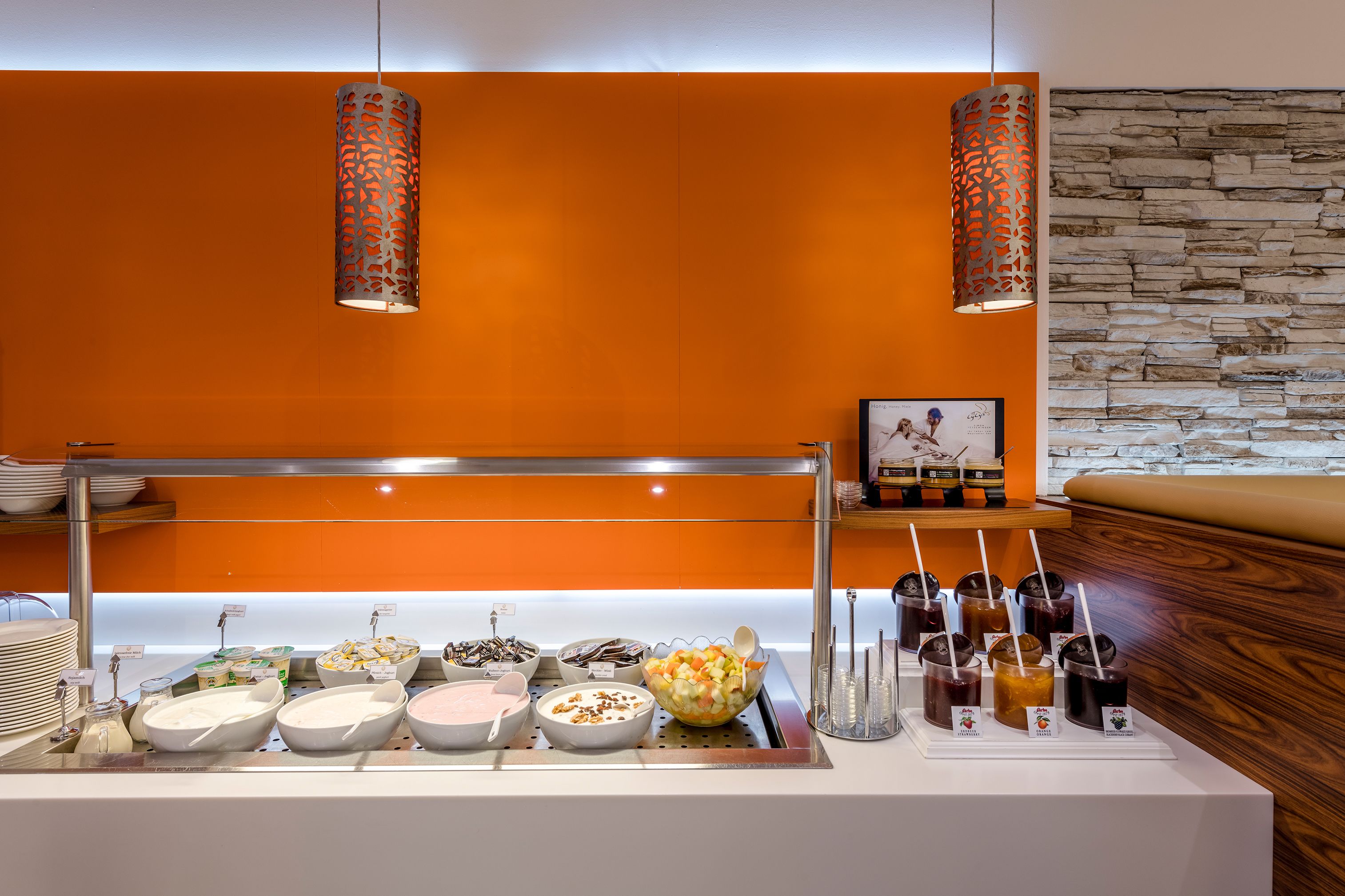 A buffet area with various food and drink options, including bowls of yogurt, a fruit bowl, and a selection of juices.