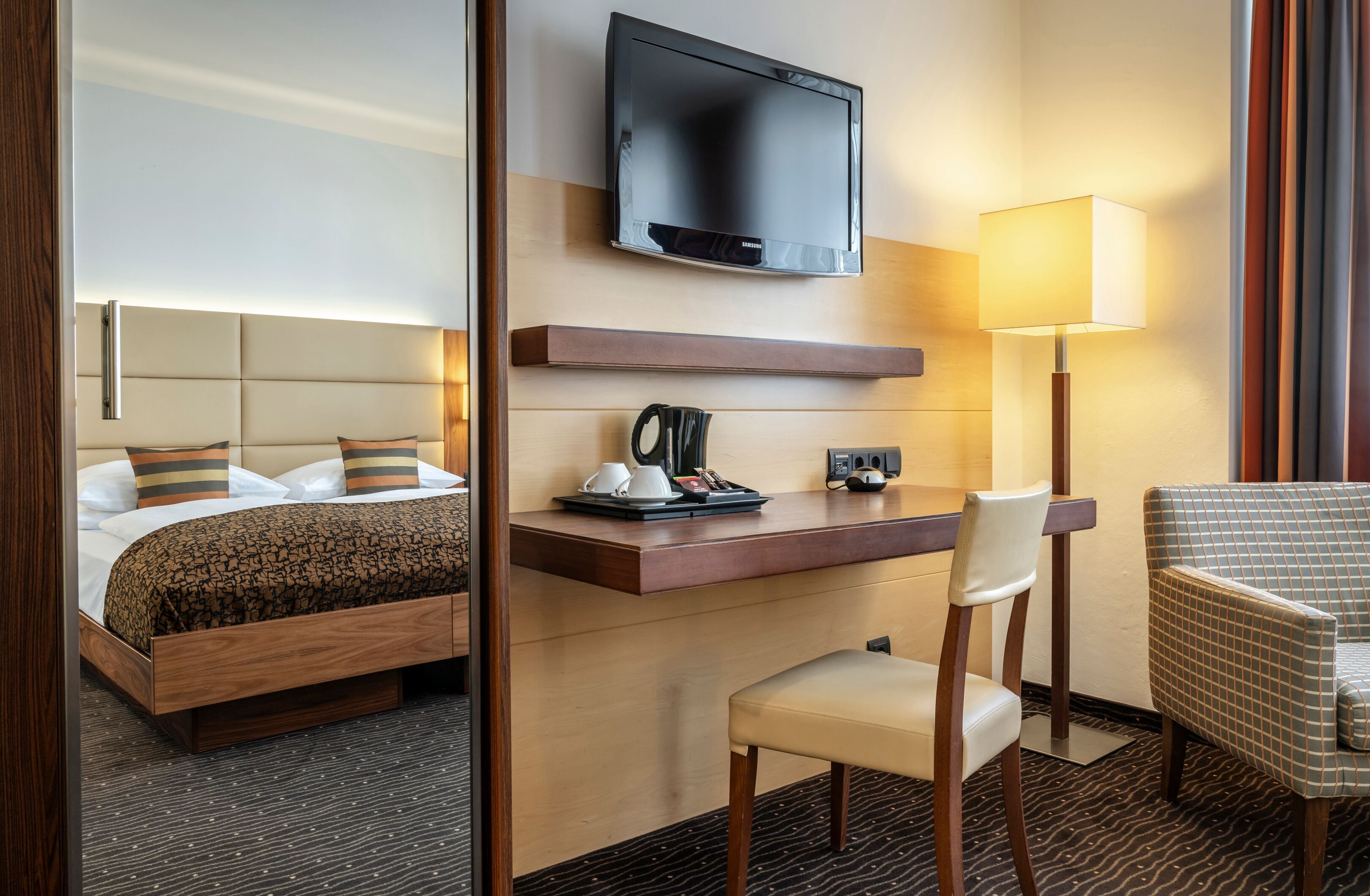 Ett hotellrum med en säng, ett skrivbord med en platt-TV, en stol och en lampa.