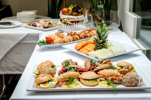 Mesa de buffet com diversos alimentos, incluindo sanduíches, doces e frutas.