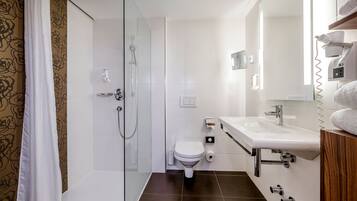 Un baño moderno con cabina de ducha de vidrio, inodoro blanco y lavamanos con espejo.