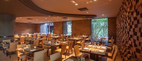 Un restaurante espacioso con varias mesas y sillas, ventanas amplias y un diseño de techo moderno.
