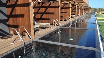 A long, narrow swimming pool with wooden deck seating and metal handrails.