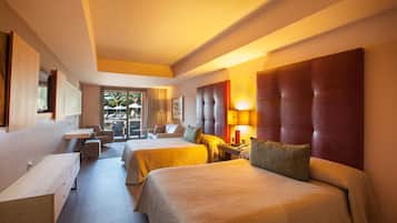 A hotel room with two beds, a desk, and a view of the outdoor area.