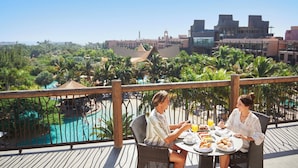 A couple dining at a table with a view of a pool and resort buildings. - Lopesan Baobab Resort (San Bartolomé de Tirajana)