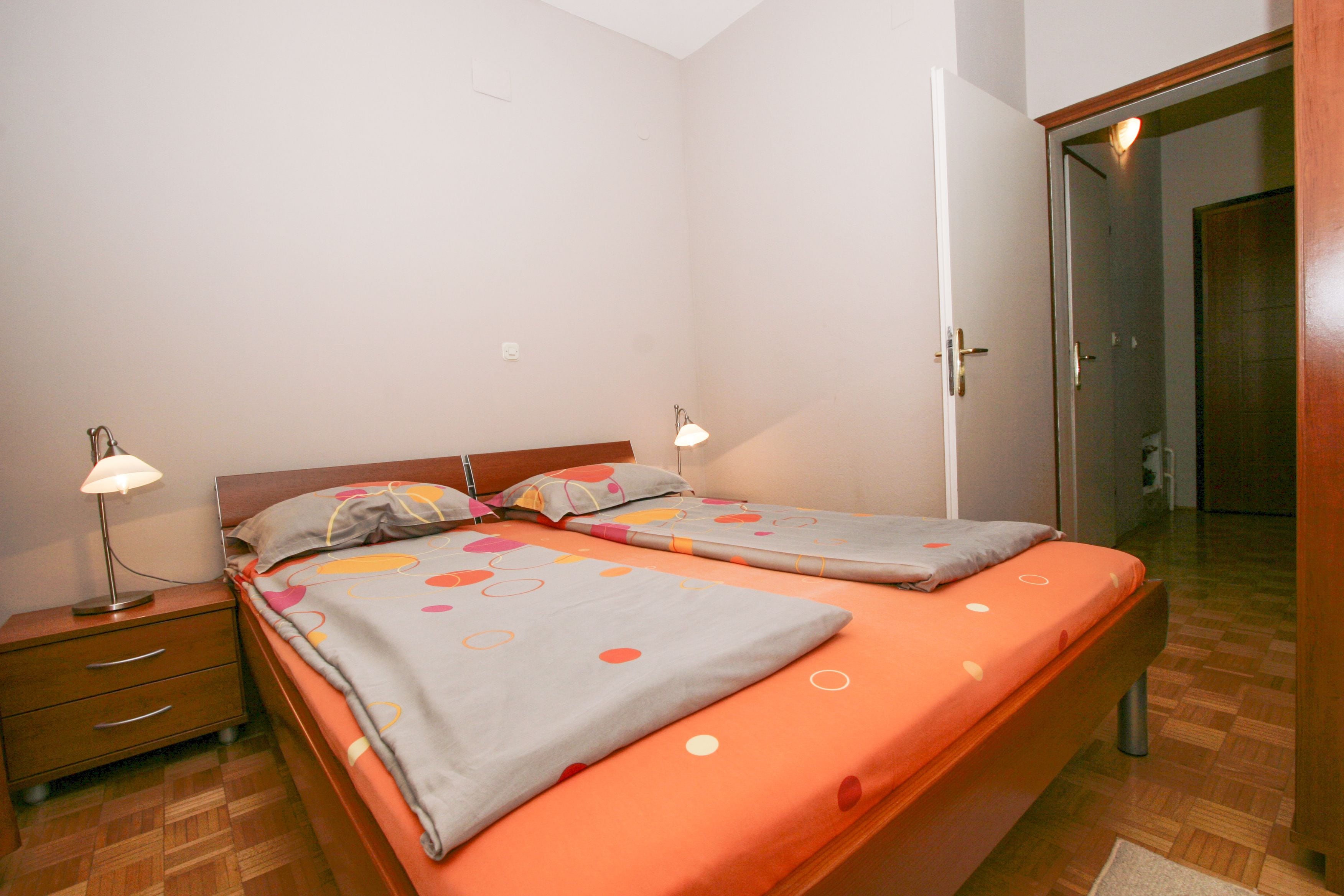 A bedroom with two single beds, a nightstand with a lamp, and a wooden wardrobe.