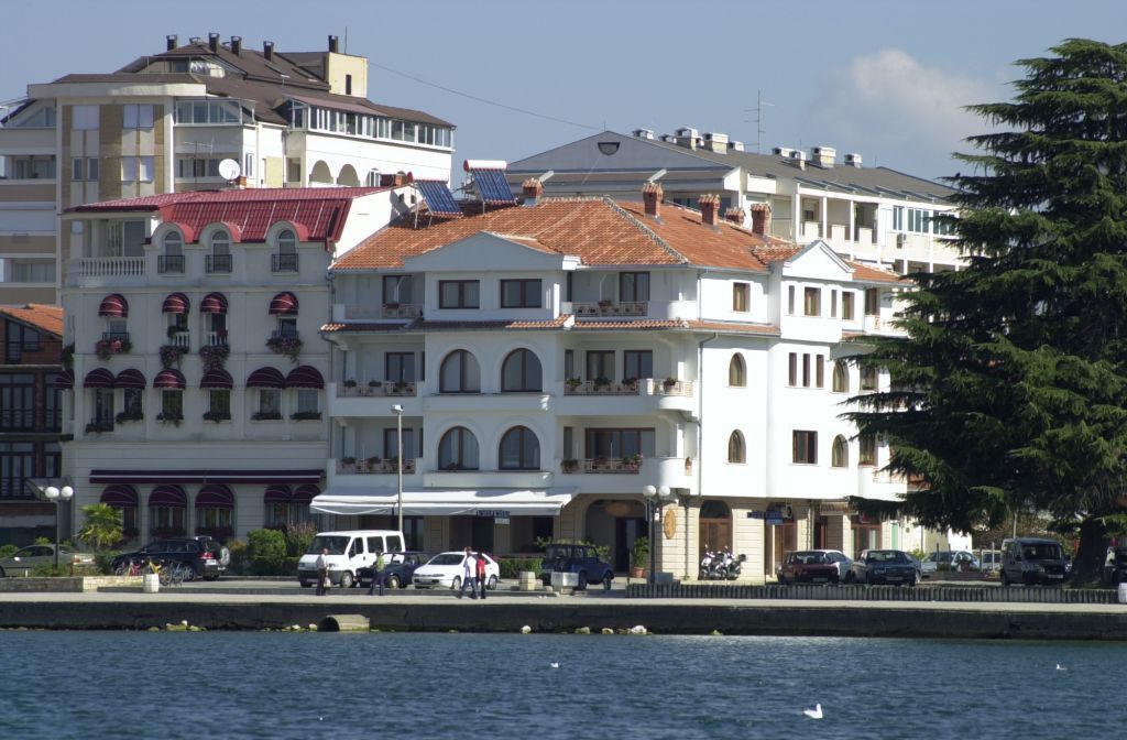A waterfront hotel with multiple stories, balconies, and a red-tiled roof.