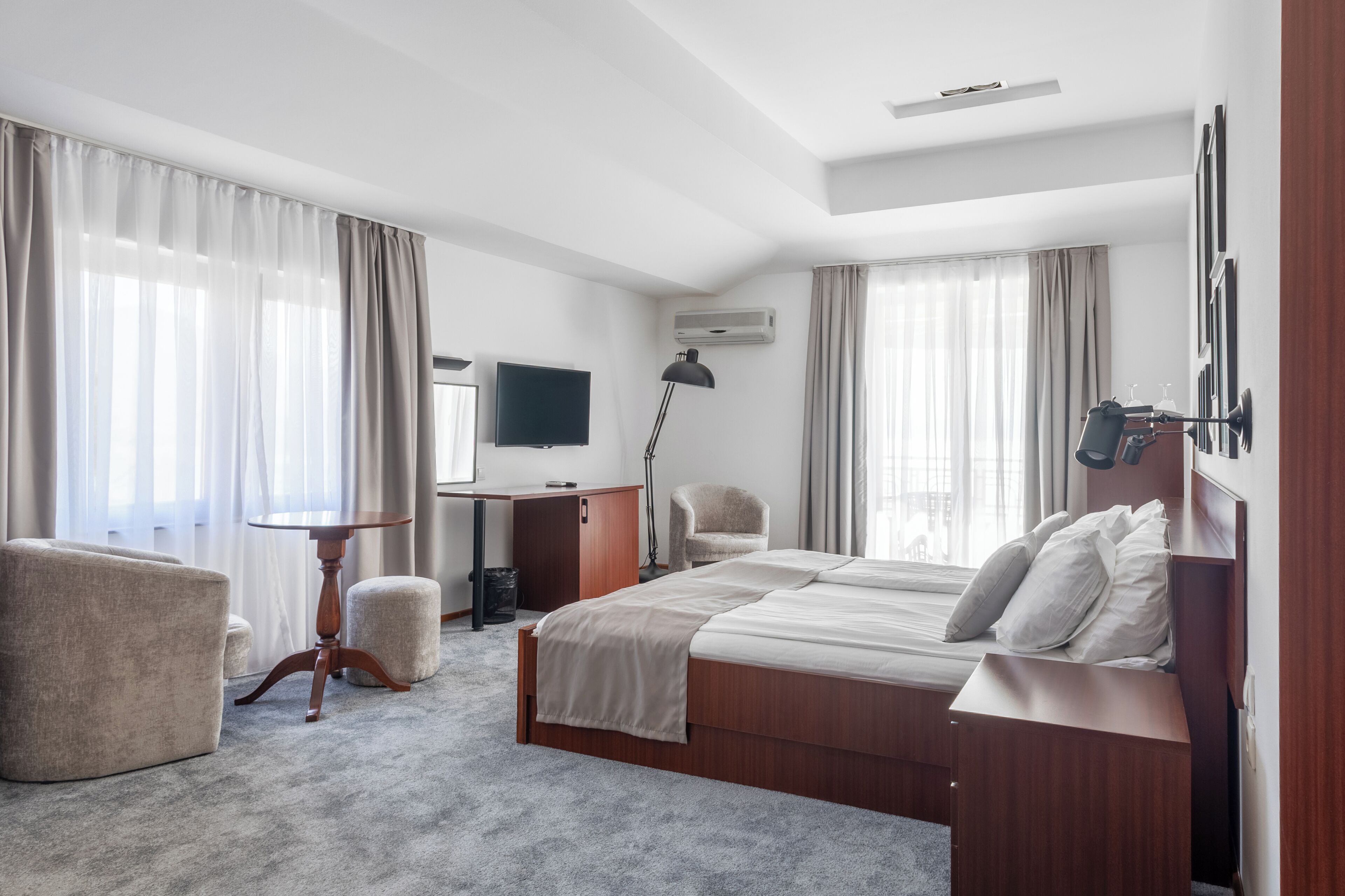 A hotel room with a bed, a desk, a chair, a TV, and a lamp.
