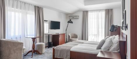 A hotel room with a bed, a desk, a chair, a TV, and a lamp.