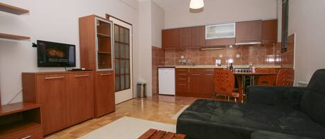A modern kitchen with wooden cabinets, a dining area with a dark sofa, and a small wooden table.