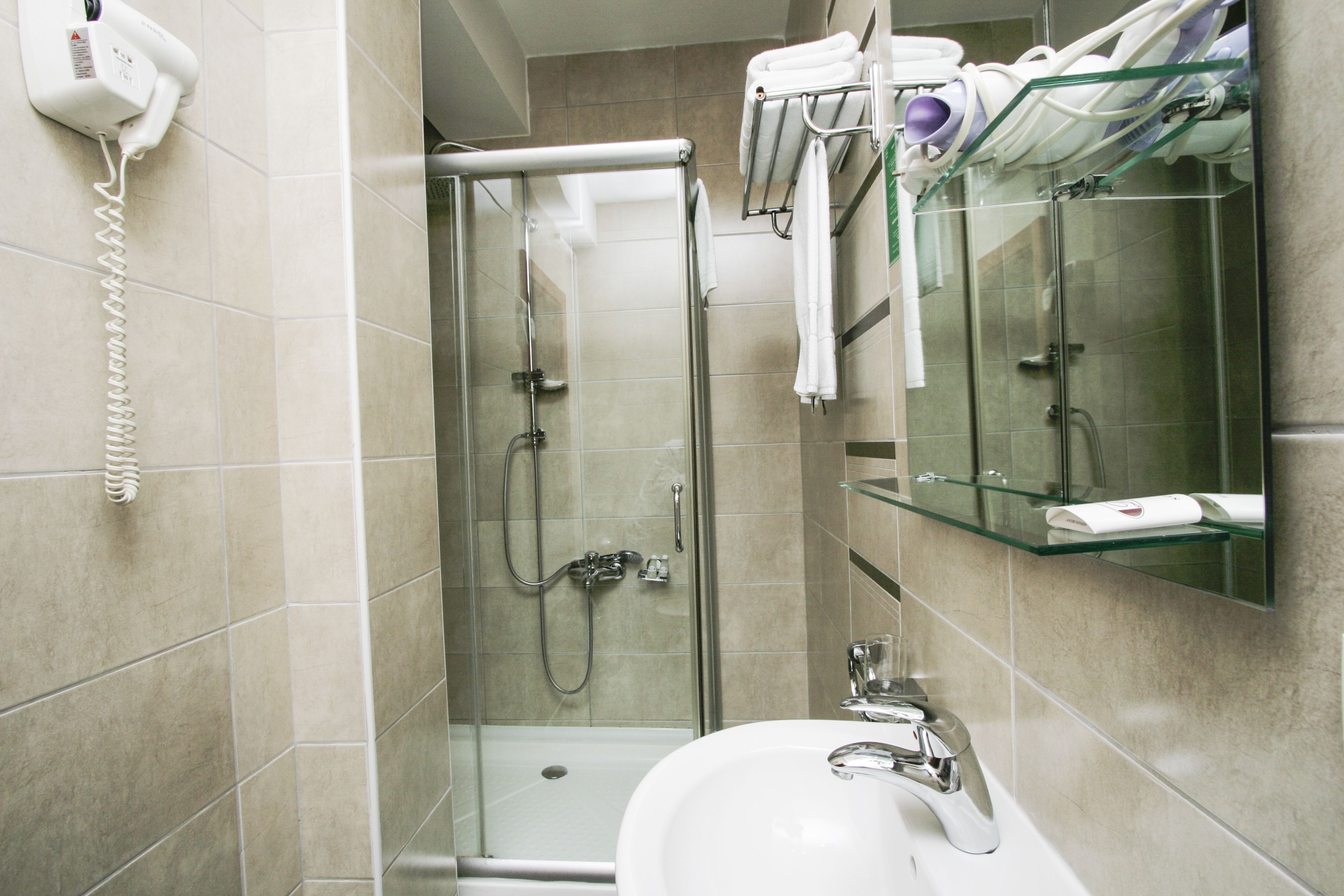 A modern bathroom with a glass-enclosed shower, a white sink, and a glass shelf above the mirror.