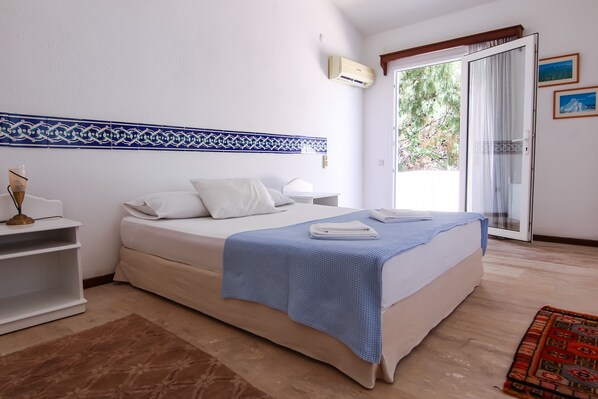 A bedroom with a bed, a nightstand, a lamp, and a window with a view of greenery.