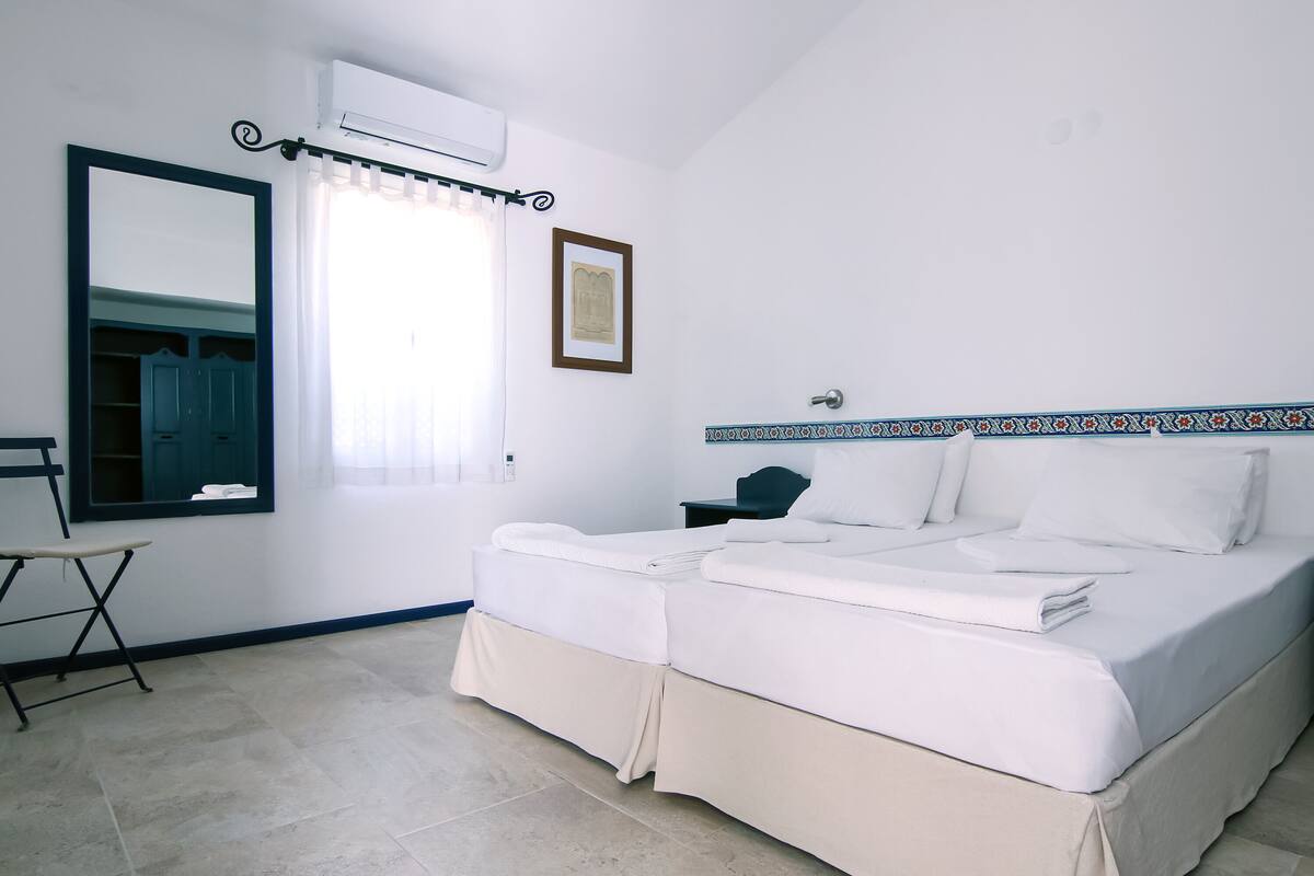 Una habitación de hotel con cama, escritorio, silla, espejo y ventana con cortinas.