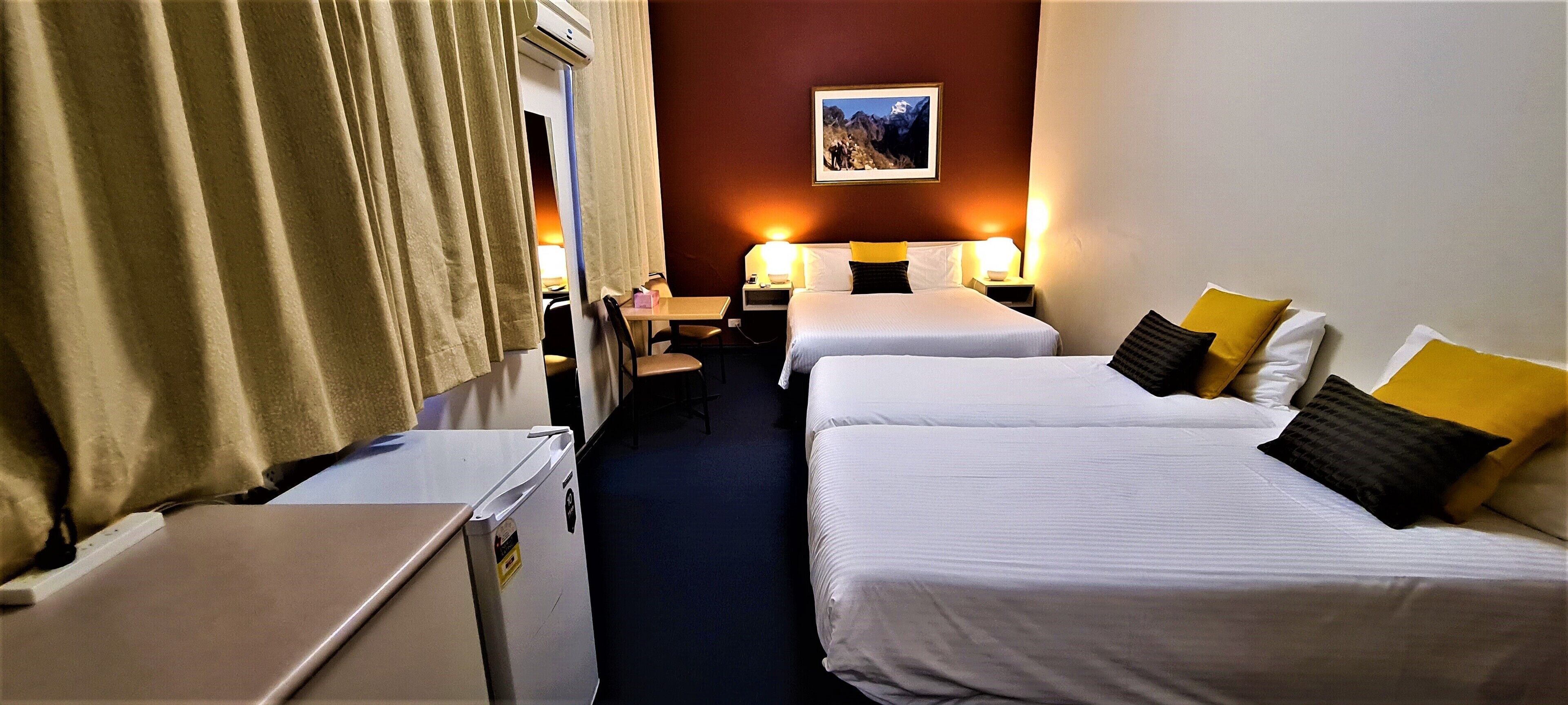 Habitació d'hotel amb dos llits individuals, una escriptori, una cadira, una taula petita i un frigorífic.