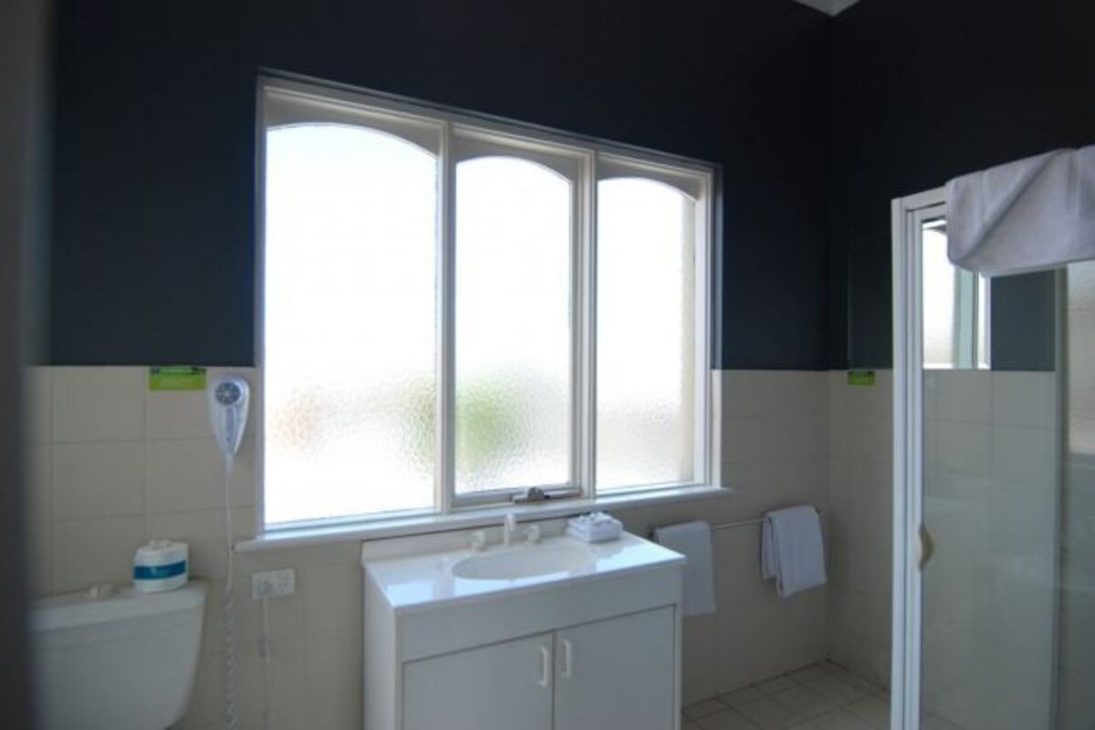 A bathroom with a window, a sink, a toilet, and a shower area.