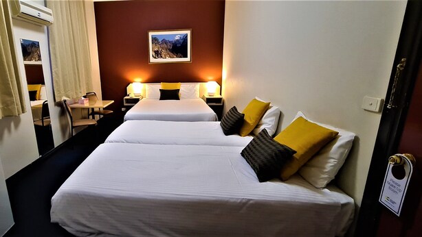 A hotel room with two beds, a desk, a chair, a small table, and a picture on the wall. - Brunswick Tower Hotel (Brunswick)
