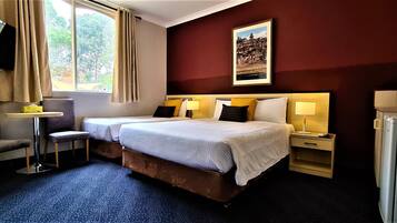 Habitación de hotel con dos camas, un televisor montado en la pared, una mesita y un escritorio con lámpara.