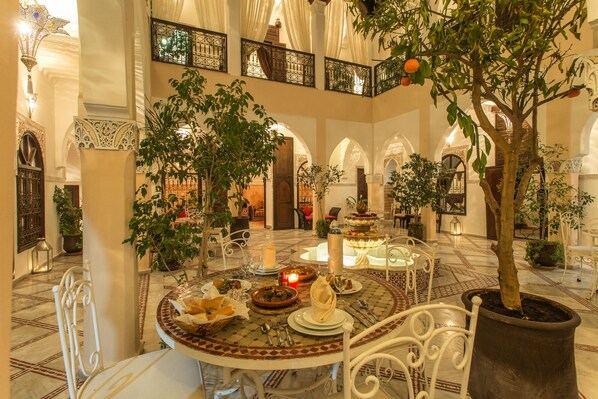 A dining area with a round table set for a meal, surrounded by white chairs.