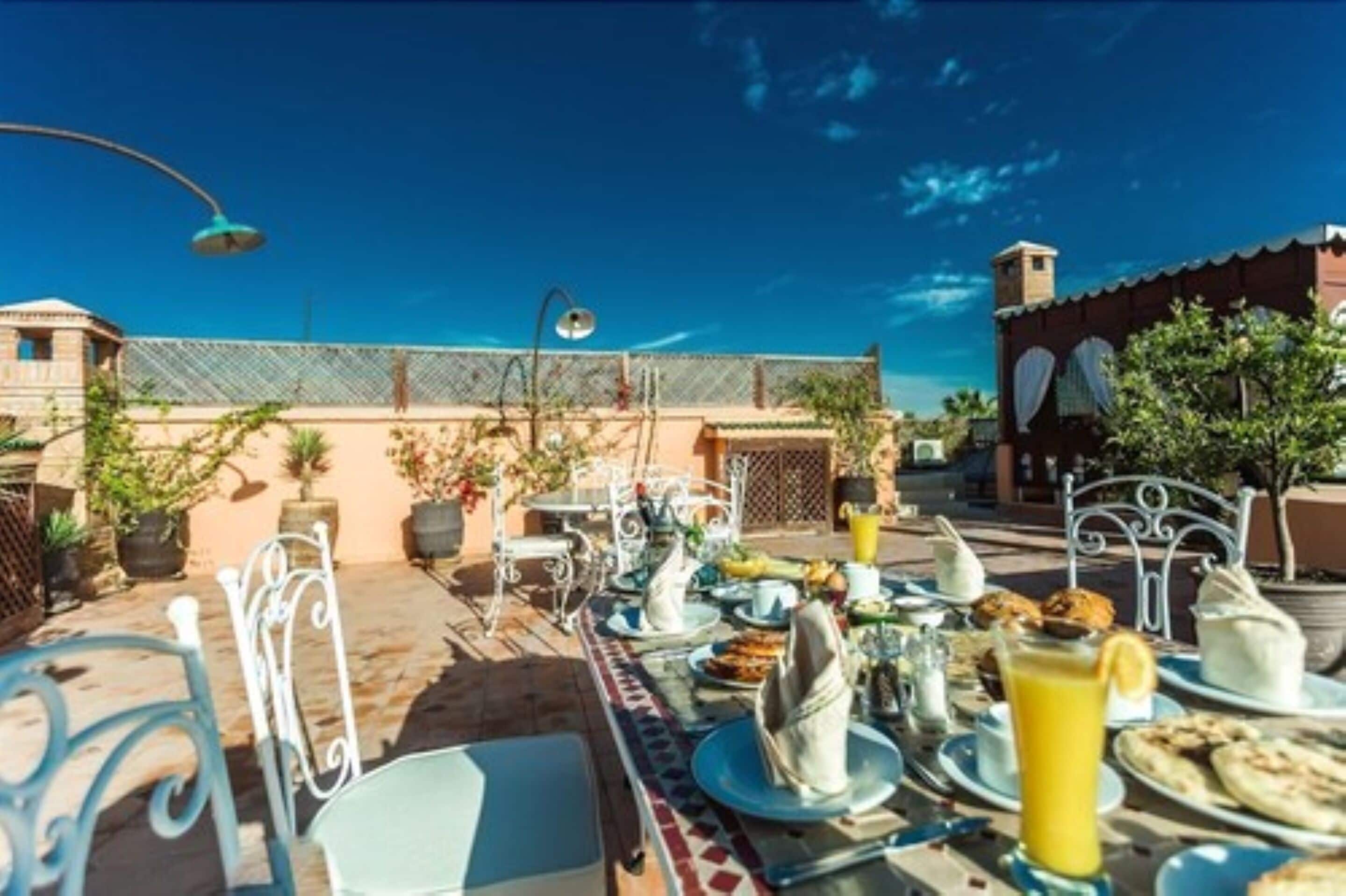 An outdoor dining area with tables set for breakfast, including plates, cups, and a pitcher of orange juice.