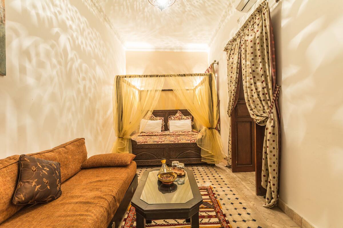 Quarto com uma cama, um sofá, uma mesa de centro e um tapete estampado.