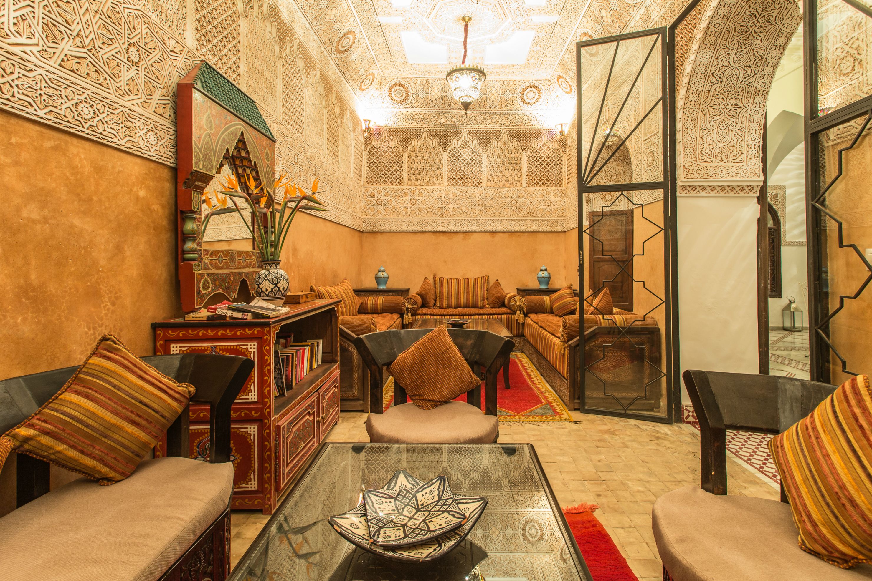 A traditional Moroccan interior with ornate patterns, a sofa set, a coffee table, and a bookshelf.