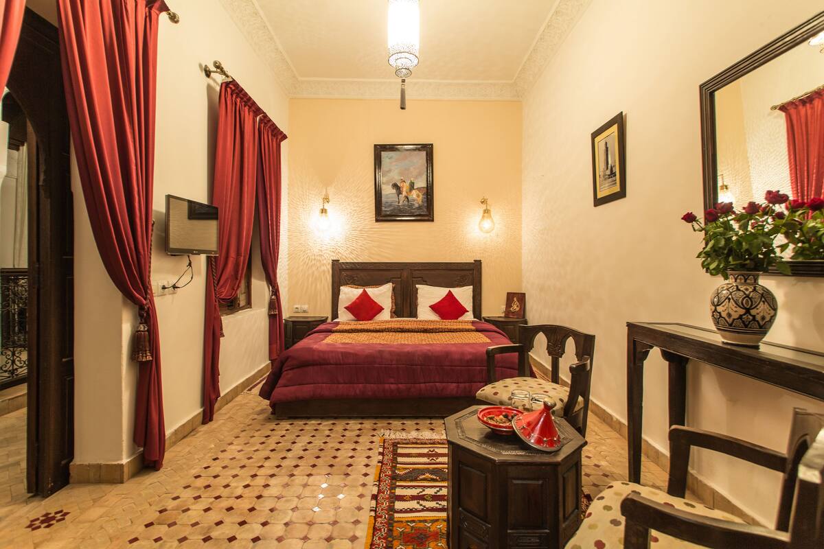Um quarto com uma cama, mesa de cabeceira, uma cadeira, uma mesa e um espelho.