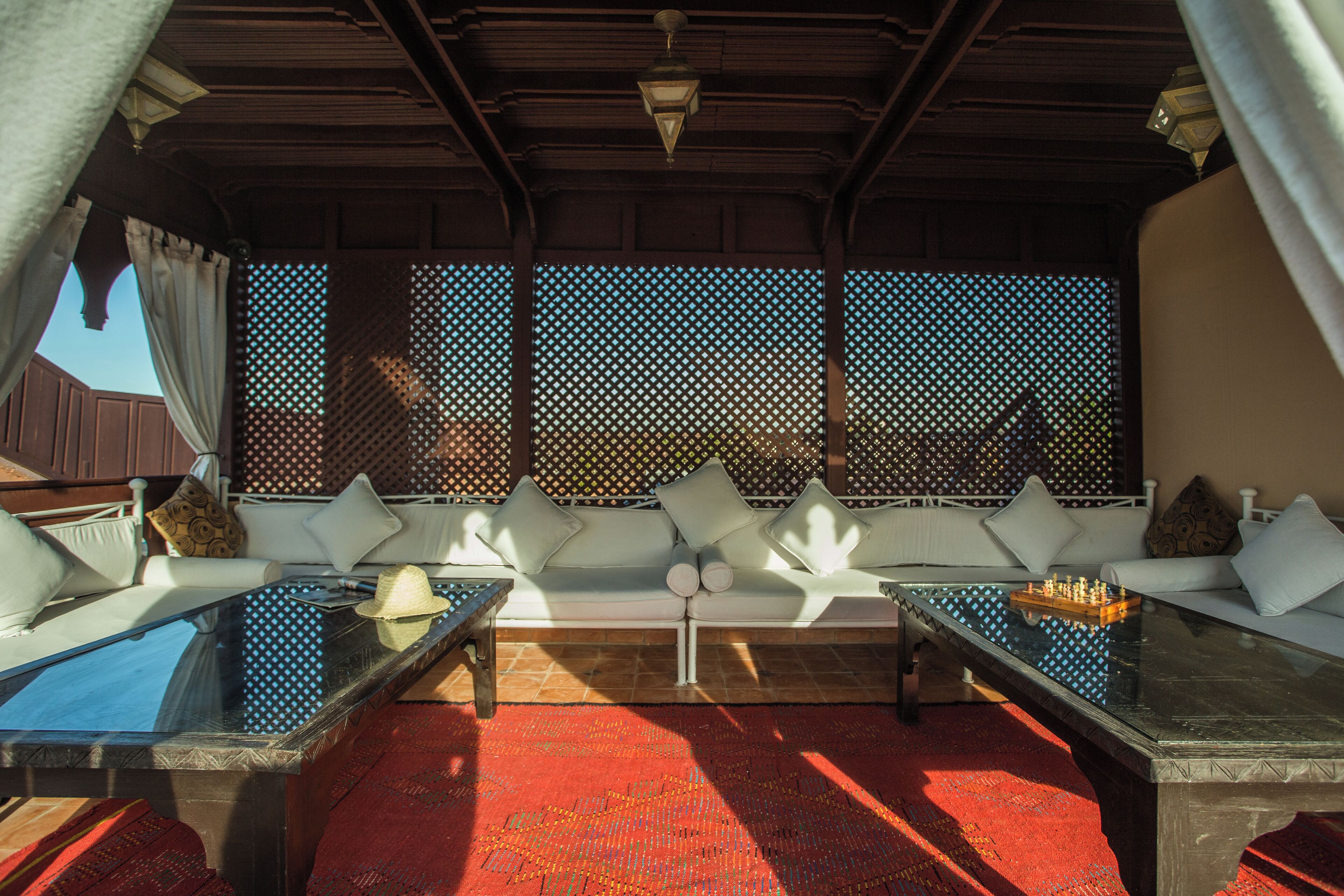 A sunlit outdoor seating area with a sofa and two tables, a patterned wall, and a wooden ceiling.