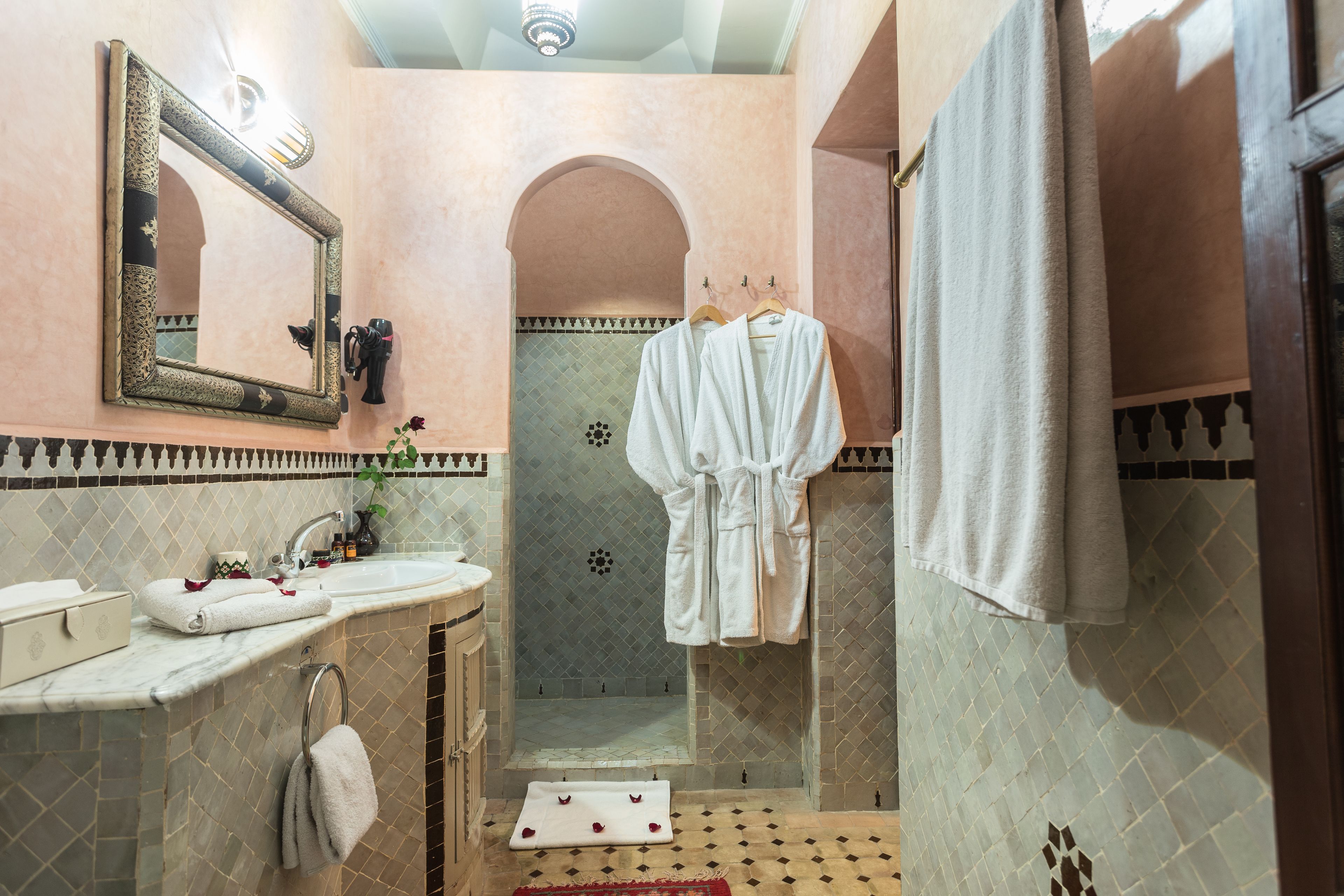 A bathroom with a sink, mirror, shower, and two towels hanging on hooks.