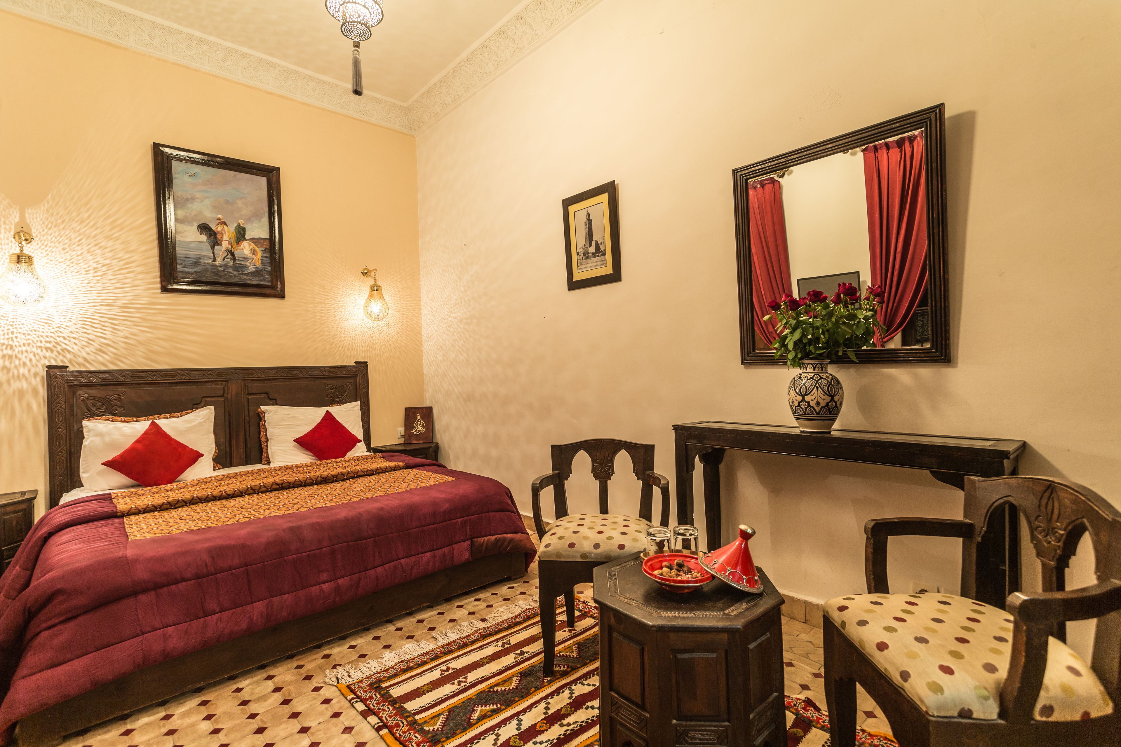 A neatly arranged bedroom with a bed, two chairs, a small table, and a mirror.