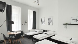 A hotel room with three single beds, a desk with a chair, a small table, and a TV. - Hotel AVAlex (Berlin)