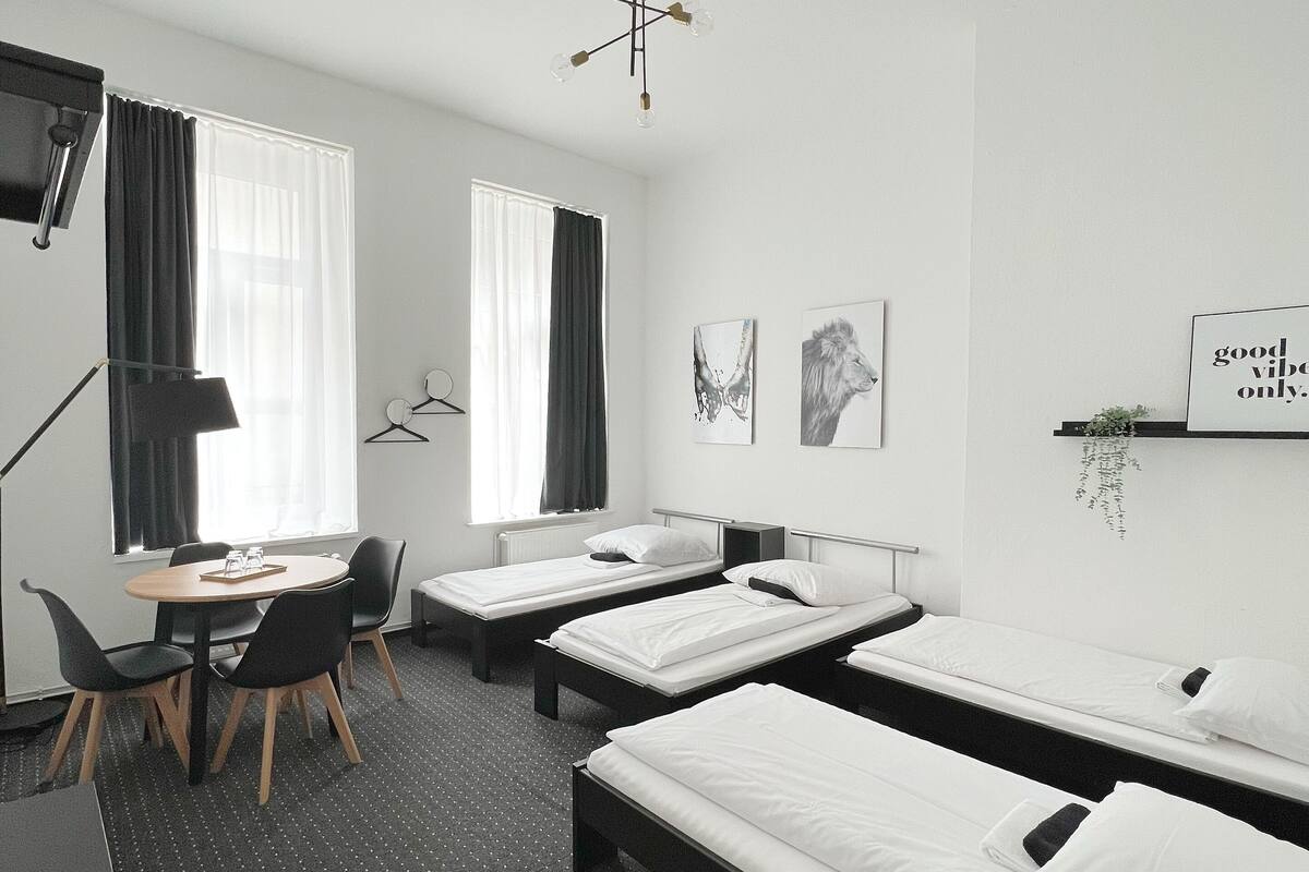 A hotel room with three single beds, a desk with a chair, a small table, and a TV.