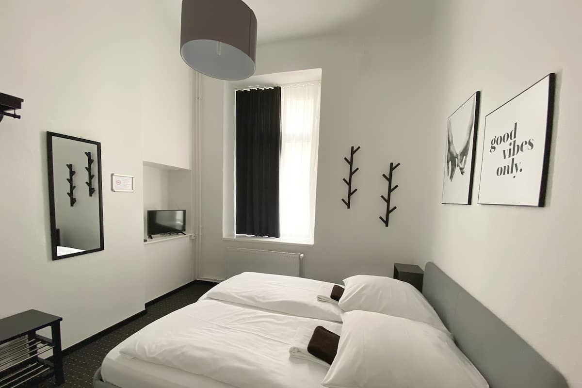 A hotel room with a bed, a TV, a window with curtains, and wall art.