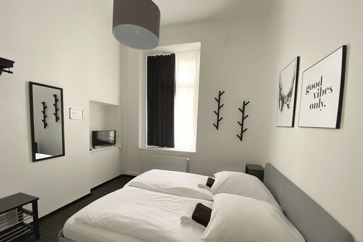 A hotel room with a bed, a television, a window with curtains, and wall art.