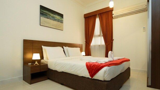 A hotel room with a large bed, a nightstand with a lamp, a painting on the wall, and a window with curtains.