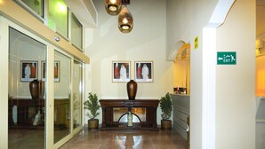 A hotel lobby with a marble floor, a reception desk, framed pictures on the wall, and exit signs.