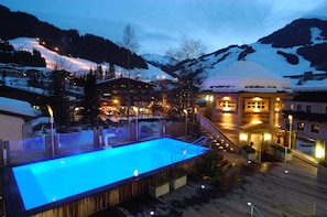 A hotel with a pool area, wooden deck, and snow-covered mountains in the background. - Hotel Alpine Palace (Saalbach-Hinterglemm)