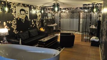 Un baño moderno con una bañera grande, un sofá negro y una pared decorativa con estampado floral.