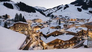 Un pueblo cubierto de nieve en la montaña, con varios edificios, incluyendo un hotel destacado con balcones y un telesilla al fondo.
