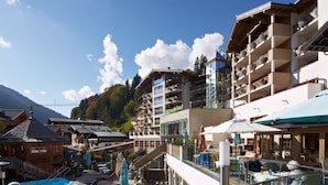 Un resort con piscina, mobiliario exterior y montañas al fondo.