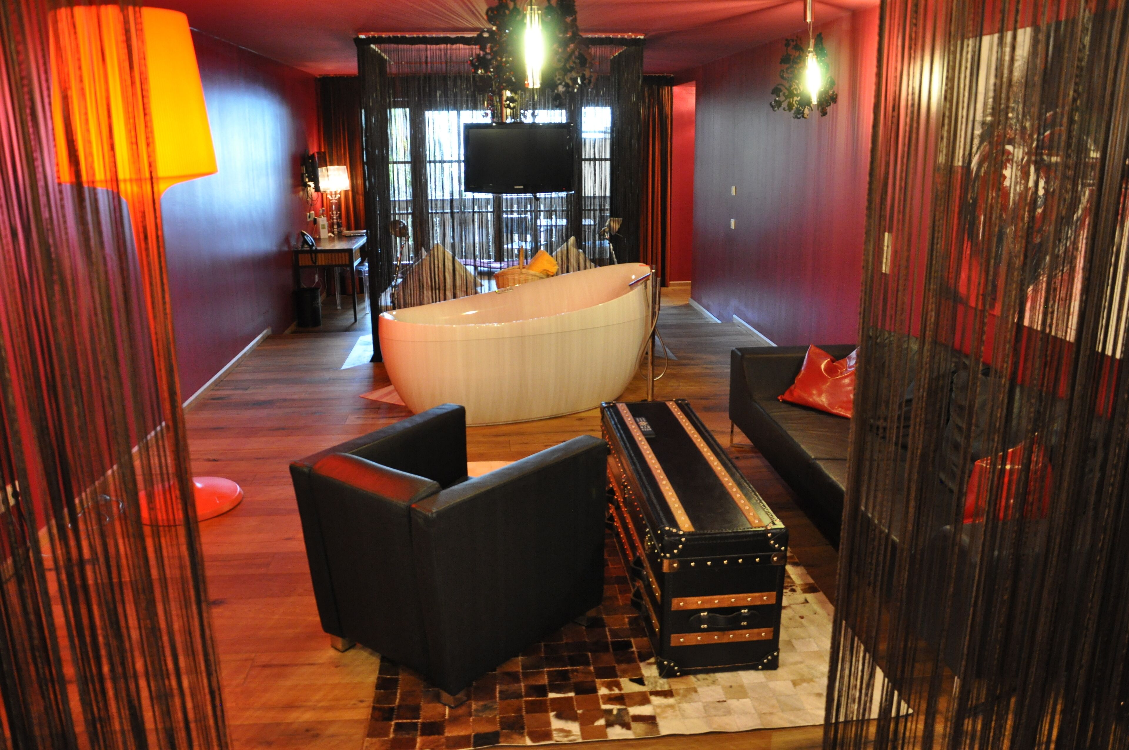 A modern bathroom with a large bathtub, black leather seating, and a vintage suitcase.