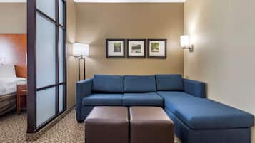 Habitación de hotel con sofá modular, cama, mesita de noche, lámpara y tres cuadros en la pared.