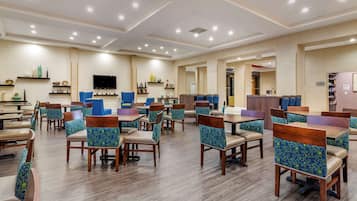 A spacious dining area with multiple tables and chairs, a flat-screen TV mounted on the wall, and a variety of decorative items on shelves.