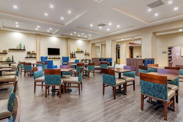 A spacious dining area with multiple tables and chairs, a flat-screen TV mounted on the wall, and a variety of decorative items on shelves. - Comfort Suites Florence I-95 (Florence)